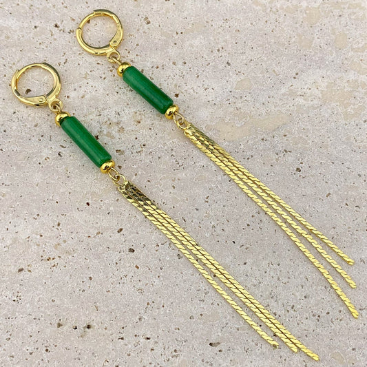 An extreme macro close-up of a Green Jade column earring on gray marble, showing the translucent dark green texture of the stone and the intricate individual links of the gold chain tassels.