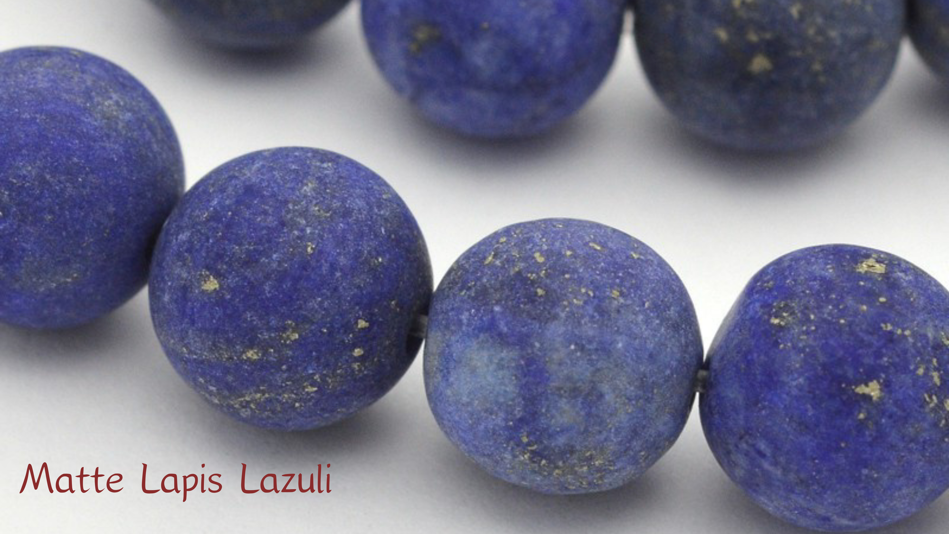 A macro close-up of matte-finished Lapis Lazuli beads showing their velvety deep blue surface and natural gold pyrite flecks; featuring the text "Matte Lapis Lazuli" neatly overlayed in the bottom right corner.