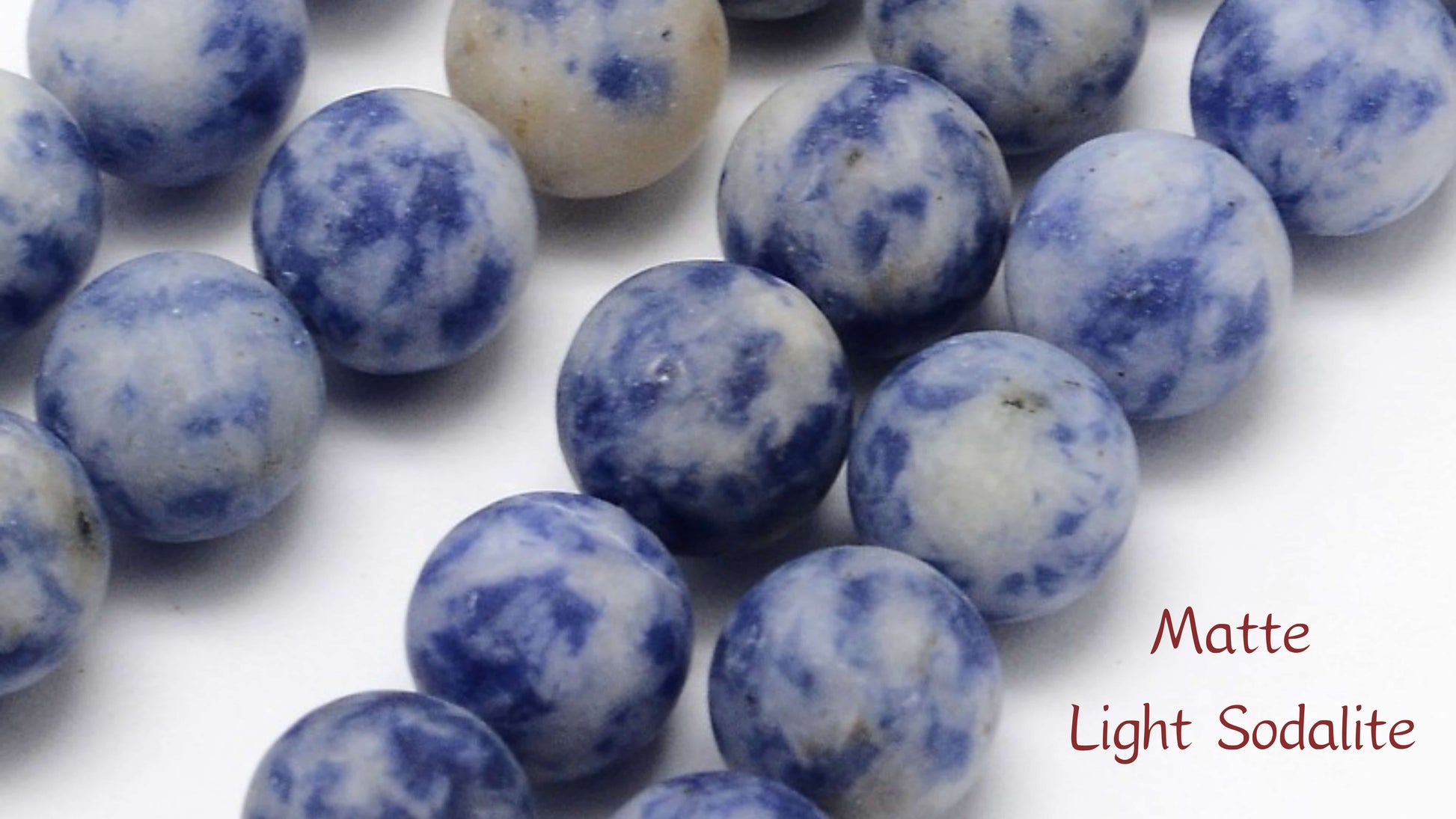 Macro close-up of Aking Sinta matte light blue Sodalite beads; the non-reflective, frosted surface shows natural white speckles and swirling patterns.