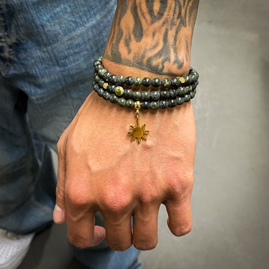 Aking Sinta Matte Serpentine Stretch Bracelet in gold worn on tattooed left hand of man, showcasing natural stone beads and stretch design