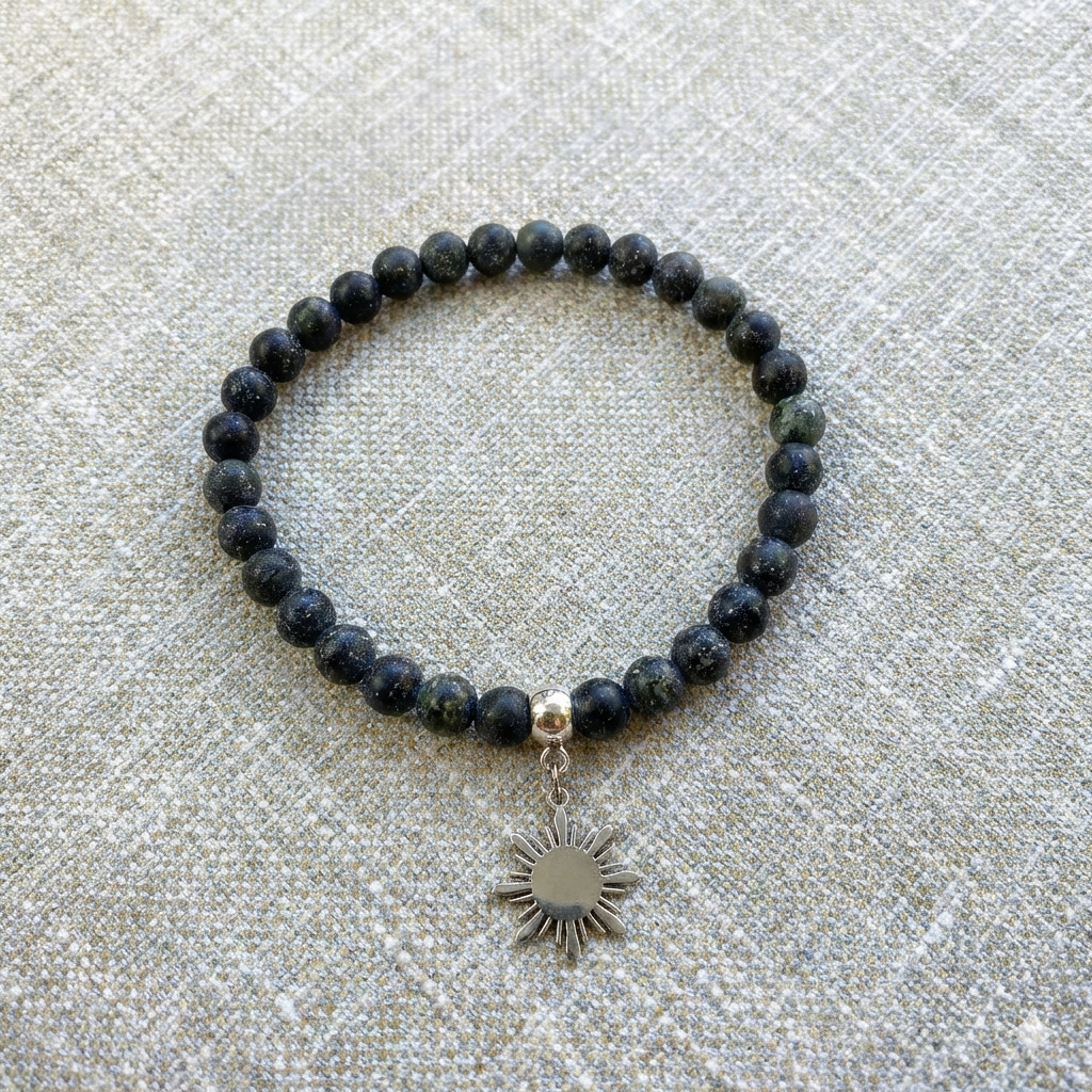 Aking Sinta Matte Serpentine Stretch Bracelet in silver with Araw charm displayed on woven grey textured background, showcasing natural stone beads and 8-ray sun motif