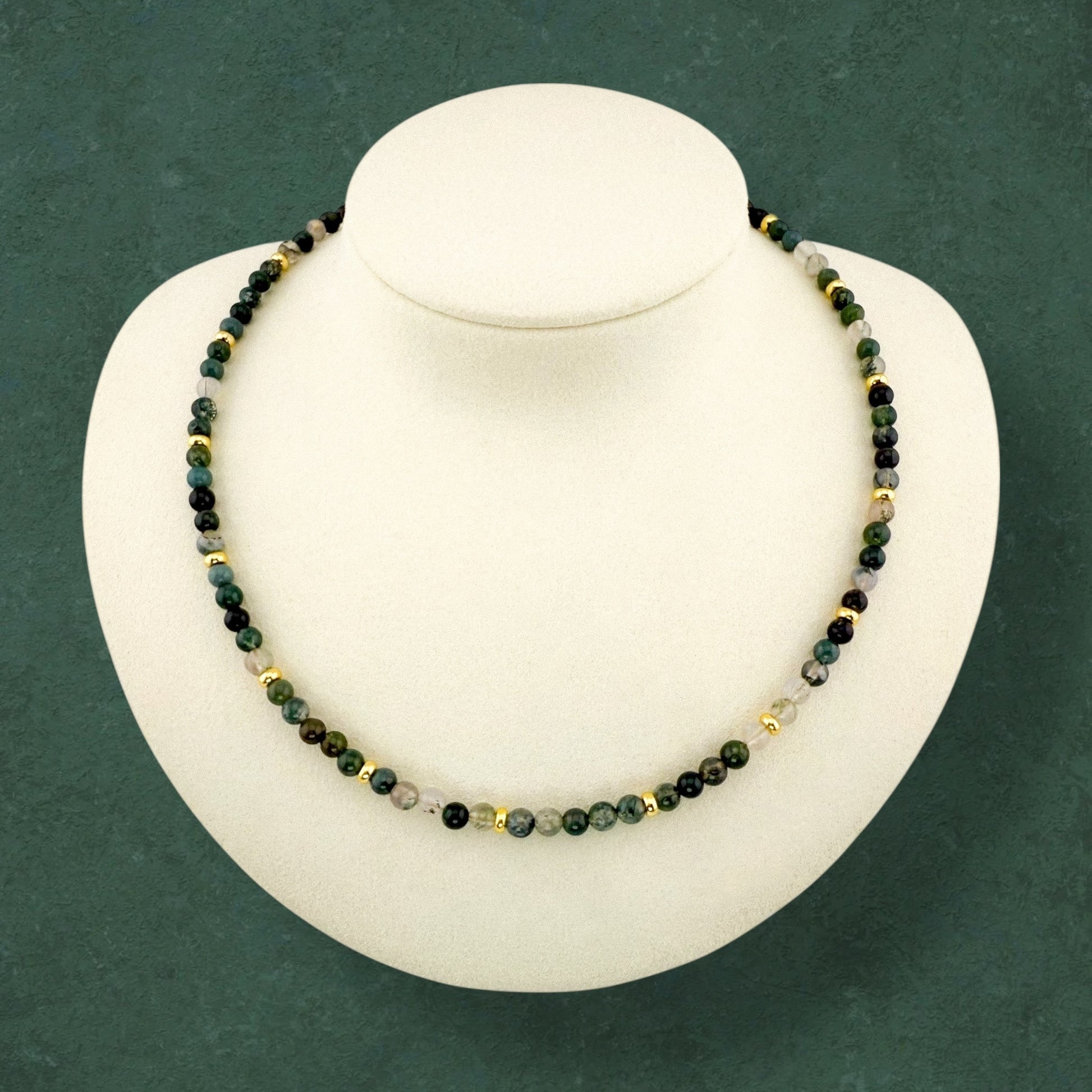 A minimalist Aking Sinta Moss Agate beaded necklace displayed on a white bust; the continuous strand features forest-green gemstones with natural mossy patterns and integrated gold accent beads, with no hanging charms or extender chain.