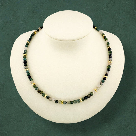 A minimalist Aking Sinta Moss Agate beaded necklace displayed on a white bust; the continuous strand features forest-green gemstones with natural mossy patterns and integrated gold accent beads, with no hanging charms or extender chain.