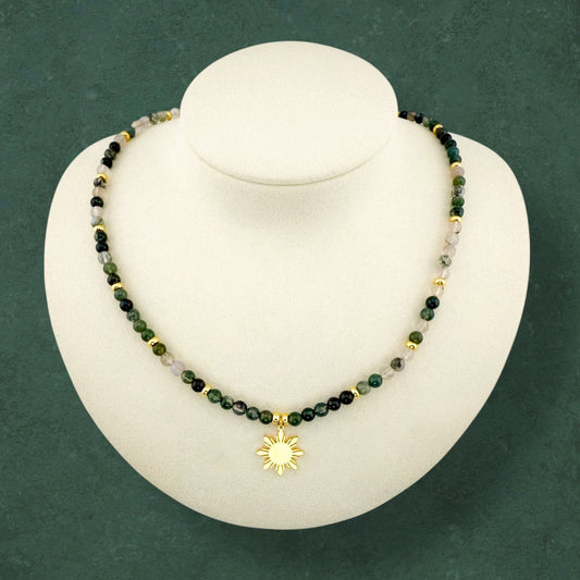 Aking Sinta Moss Agate beaded necklace on a white display bust; the strand features deep forest-green and translucent white gemstones with natural moss-like inclusions, accented by polished gold beads throughout the strand and a central 8-ray Araw sun charm.