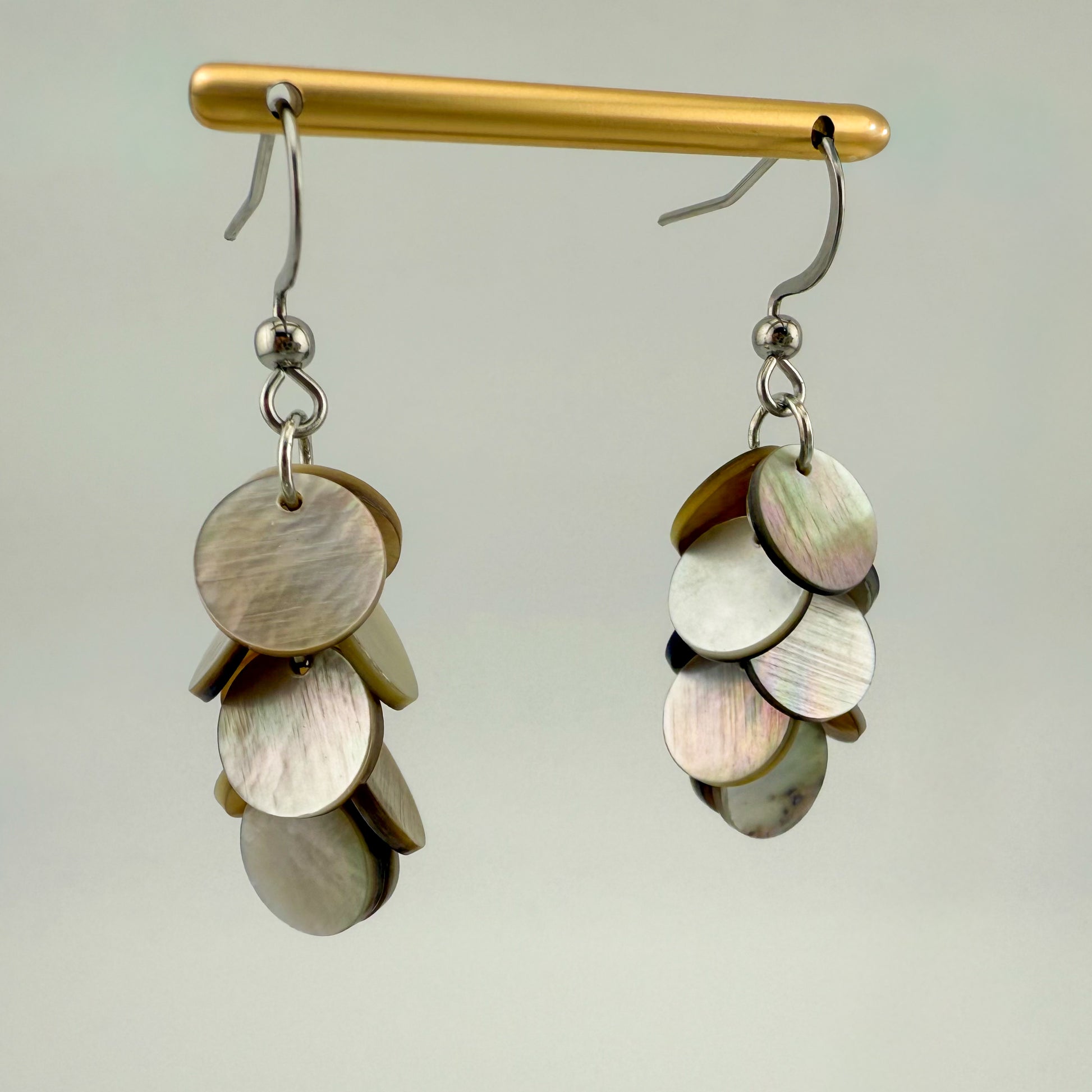 Aking Sinta dainty hook earrings featuring a cascading tier of iridescent Mother of Pearl discs on a minimalist gold wire, displayed on a white background.