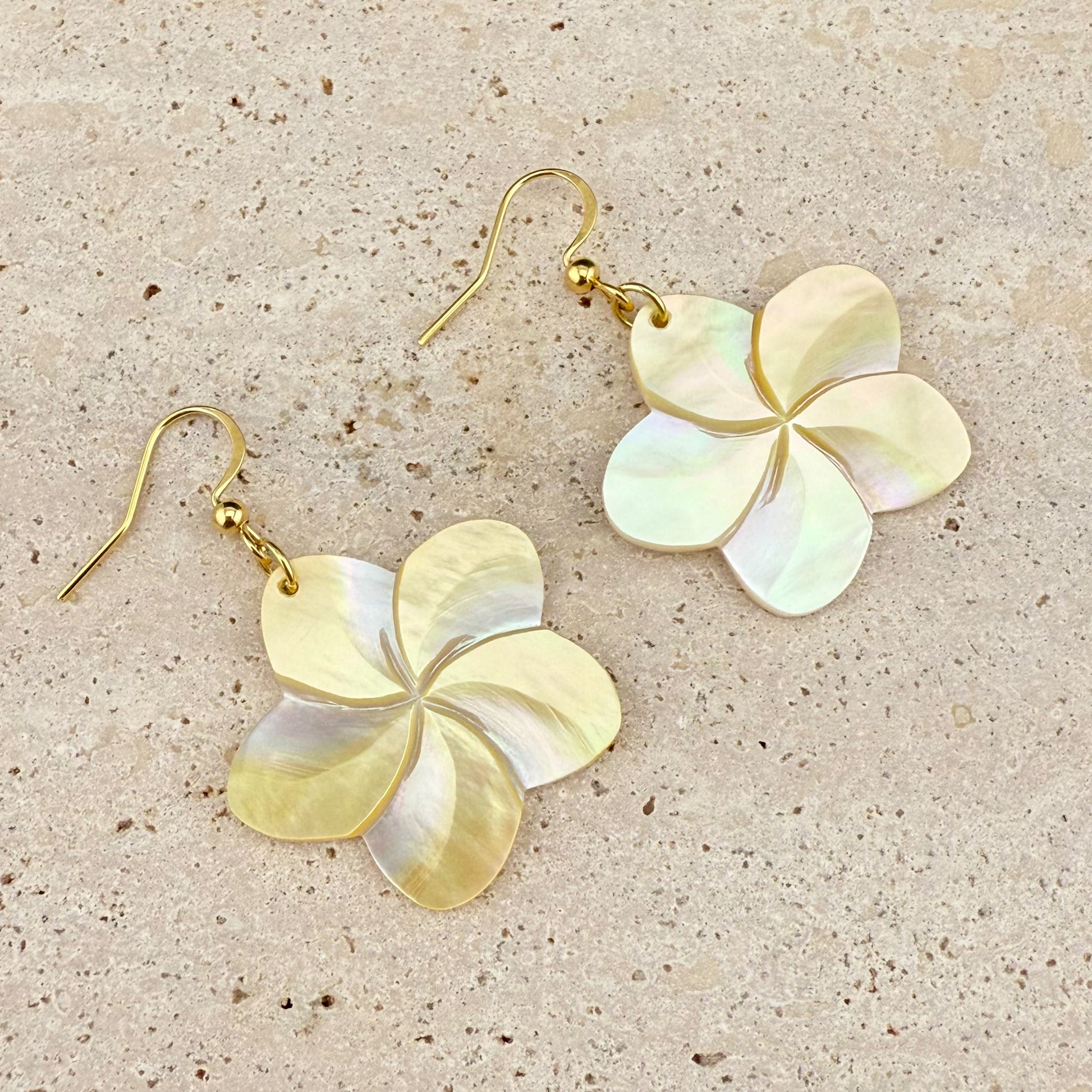 Aking Sinta Mother of Pearl Kalachuchi flower earrings with long gold hooks, displayed on a white marble-like slab; featuring hand-carved iridescent petals.