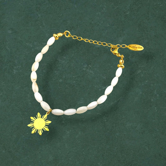 Aking Sinta Mother of Pearl Rice Bracelet with Araw sun charm displayed on dark green background, highlighting natural stone beads and Philippine-inspired design