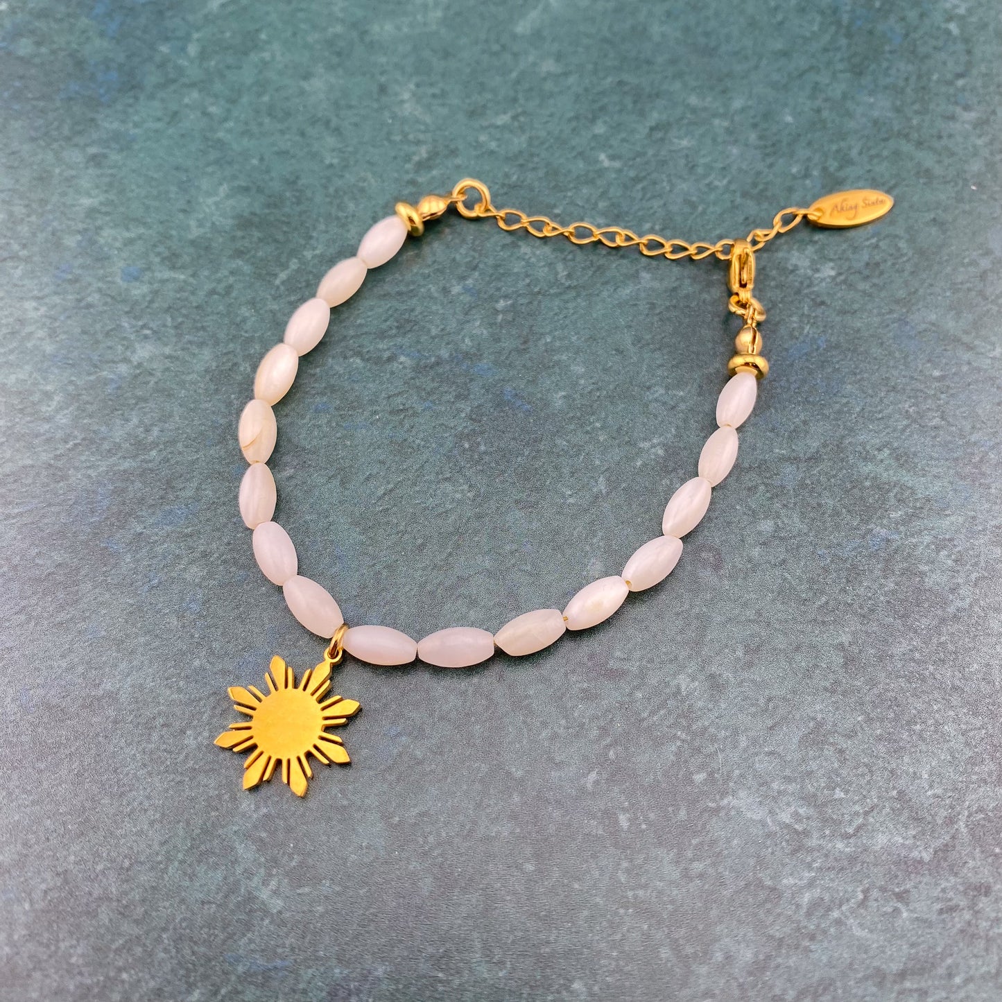 Aking Sinta Mother of Pearl Rice Bracelet with Araw sun charm displayed on gray marble textured background, highlighting natural stone beads and Philippine-inspired design