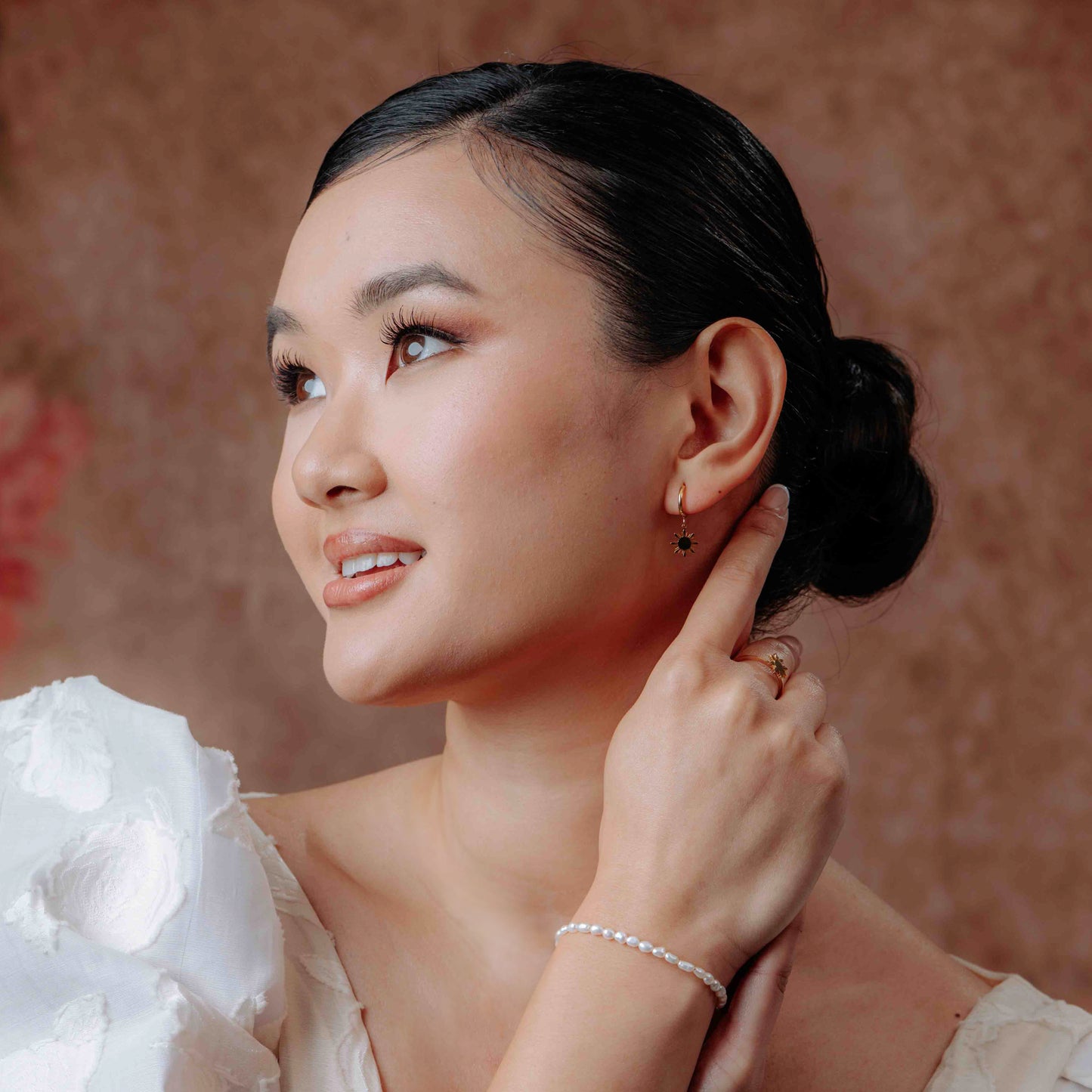 A model in profile facing left, wearing the Aking Sinta Mother of Pearl Rice Bracelet on their left wrist with their hand resting on their ear.