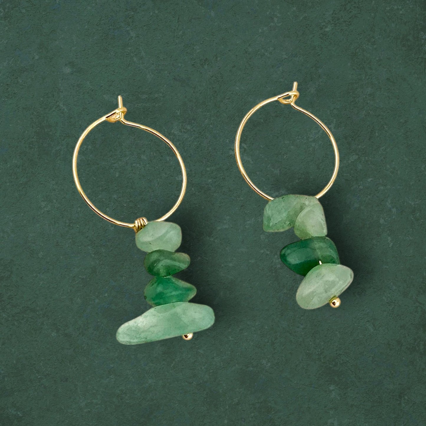 A pair of Aking Sinta gold earrings featuring a cluster of several small, raw Green Aventurine nuggets suspended in a vertical drop, displayed against a dark forest-green background.