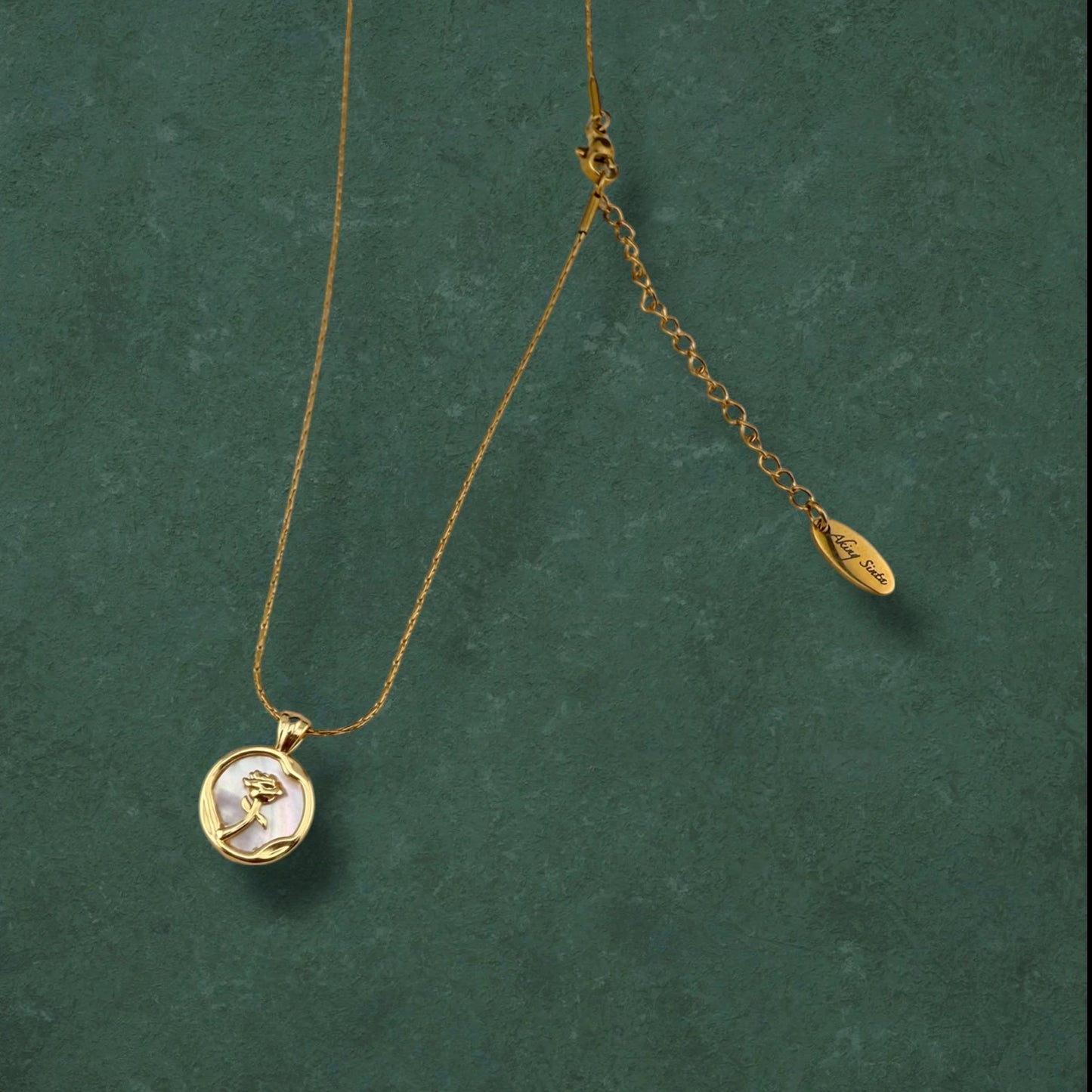 Close-up of the Aking Sinta necklace extender featuring a gold teardrop charm with "Aking Sinta" engraved, displayed on a white marble surface.