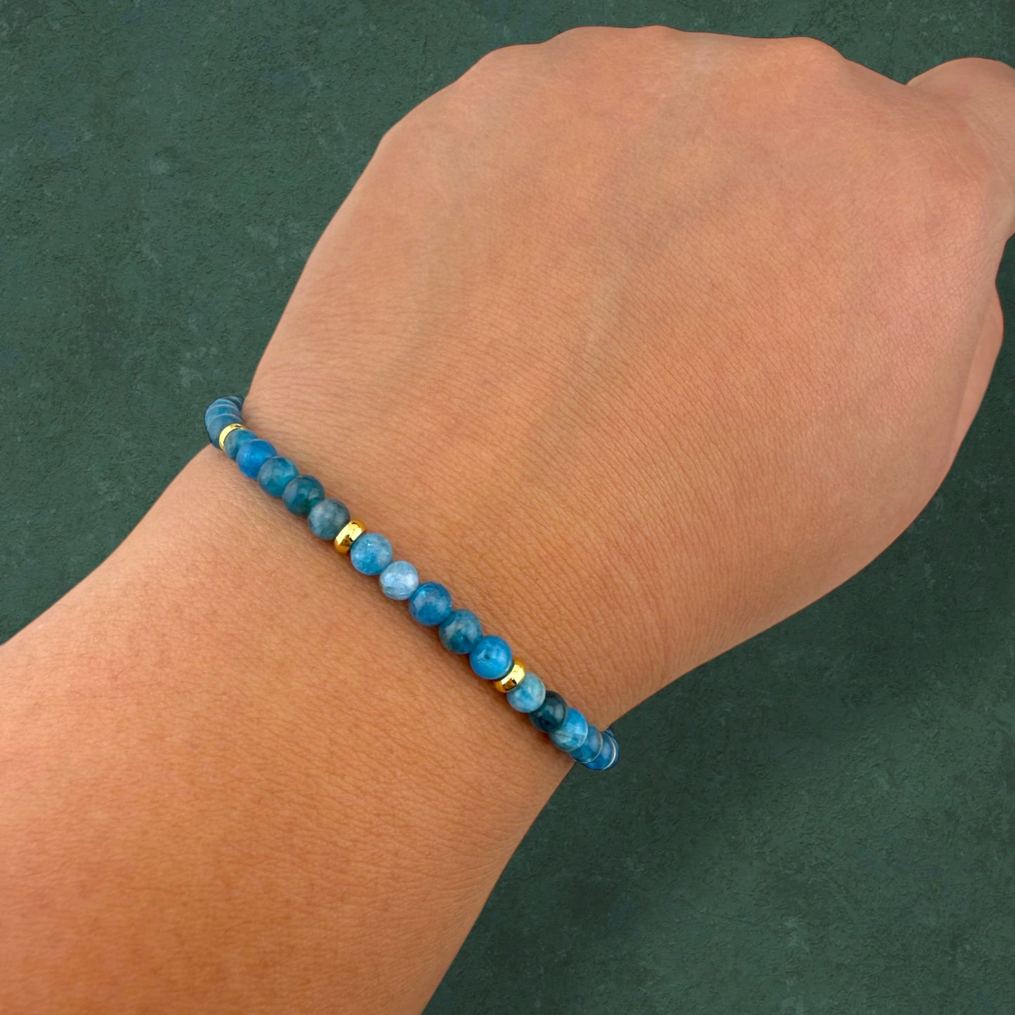 A close-up of an Aking Sinta Apatite beaded bracelet worn on a clenched fist; the vibrant, neon-blue gemstones are the main focus, showcasing their intense color and natural clarity in a bold, unisex lifestyle pose.