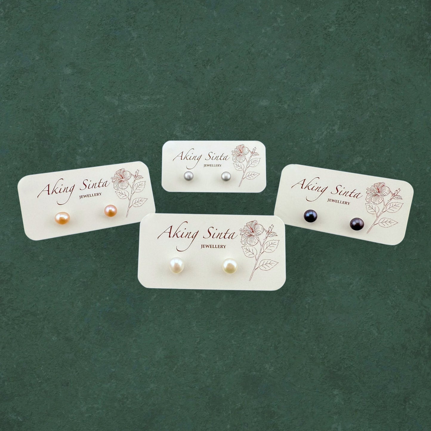 Four pairs of Aking Sinta Palawan Pearl Studs in White, Peach, Black, and Silver, displayed on a branded white jewelry card.