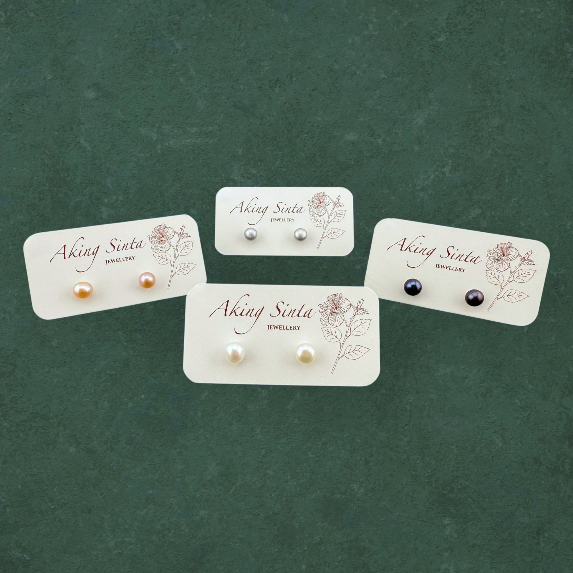 Four pairs of Aking Sinta Palawan Pearl Studs in White, Peach, Black, and Silver, displayed on a branded white jewelry card.