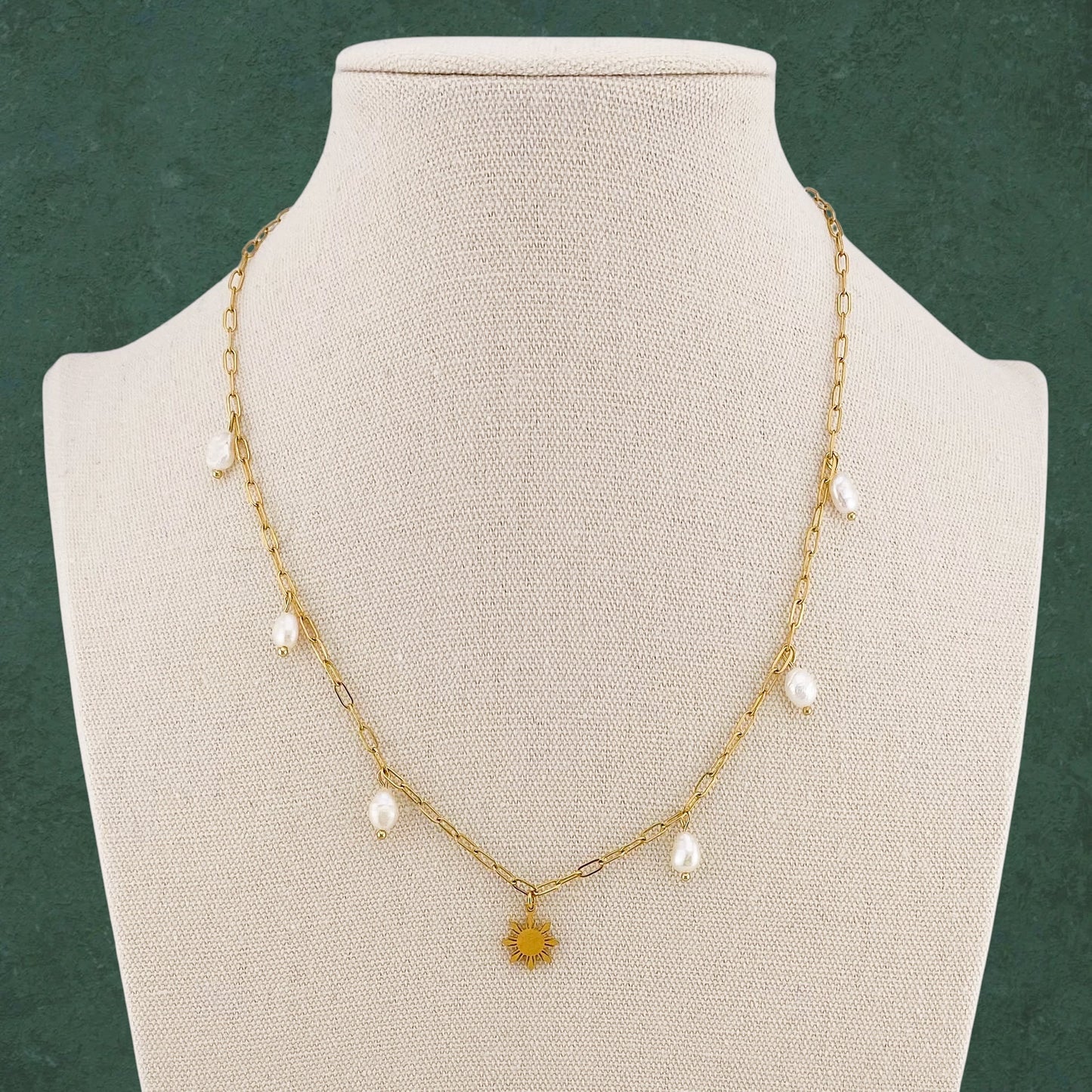 Aking Sinta Paperclip Chain Necklace with dainty Araw sun and freshwater pearl charms displayed on neck-shaped jewellery holder on dark green background, highlighting delicate design and Philippine-inspired craftsmanship