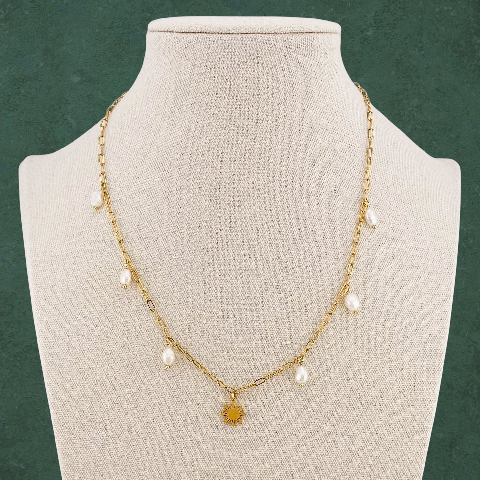 Aking Sinta Paperclip Chain Necklace with dainty Araw sun and freshwater pearl charms displayed on neck-shaped jewellery holder on dark green background, highlighting delicate design and Philippine-inspired craftsmanship