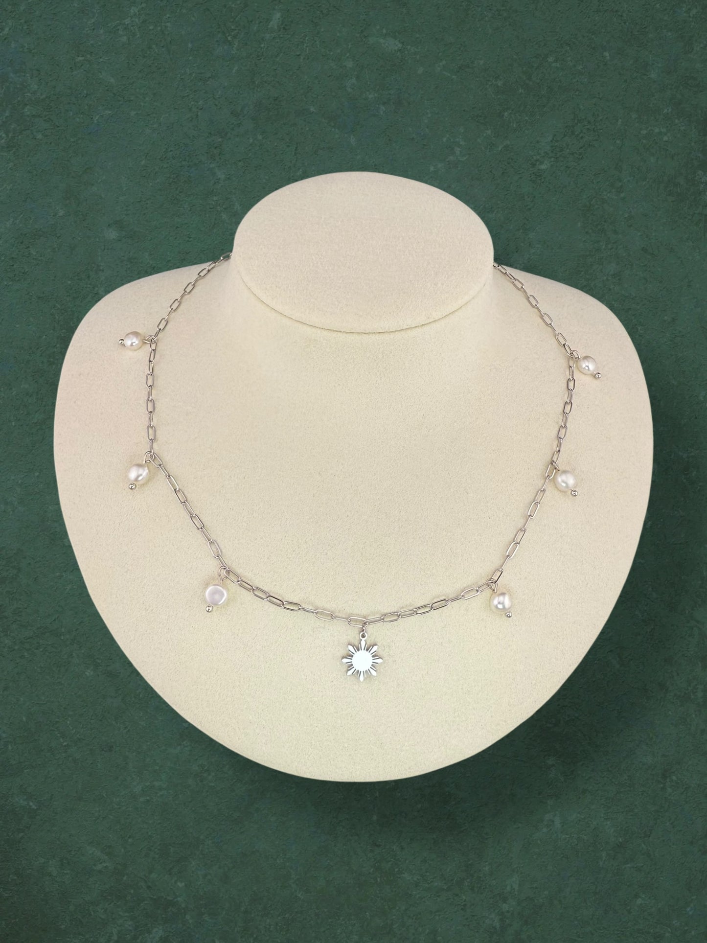 Aking Sinta Paperclip Chain Necklace silver variant with dainty Araw sun and freshwater pearl charms displayed on neck-shaped jewellery holder on dark green background, highlighting delicate design and Philippine-inspired craftsmanship