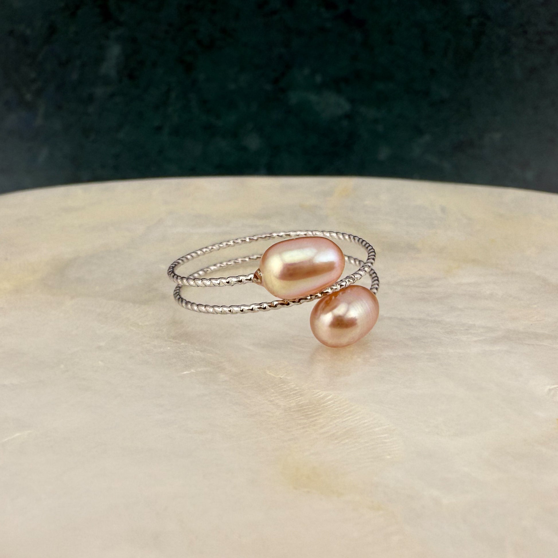 Close-up of an Aking Sinta peach double pearl adjustable ring on a white marble slab; featuring two warm apricot-toned pearls and a dainty gold band.