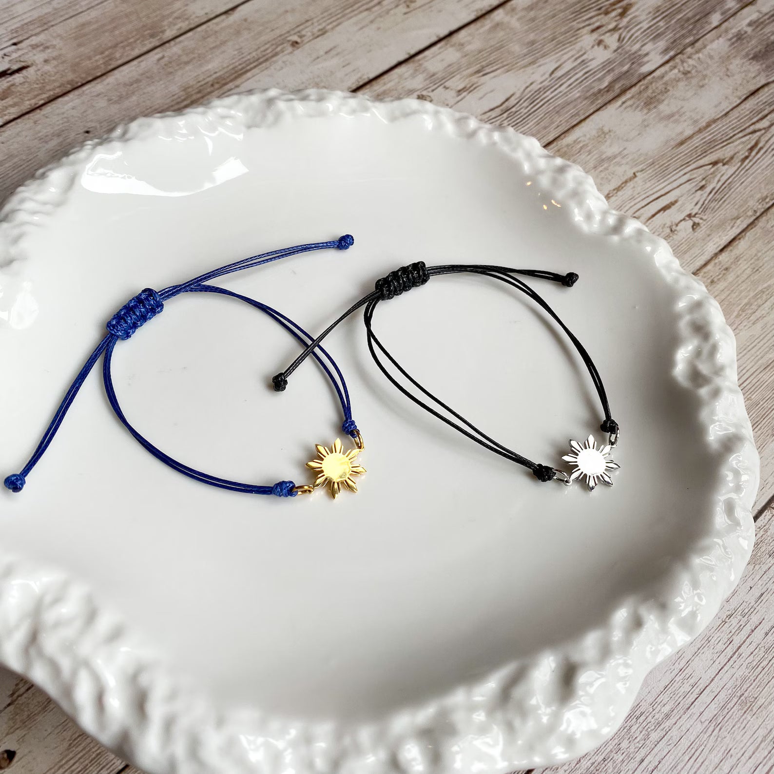 A pair of Aking Sinta Simple Philippine Sun Unisex Friendship Bracelets featuring a silver 8-ray Araw charm and a gold 8-ray Araw charm; both displayed inside a shimmering, iridescent Mother of Pearl shell container for a luxury coastal aesthetic.