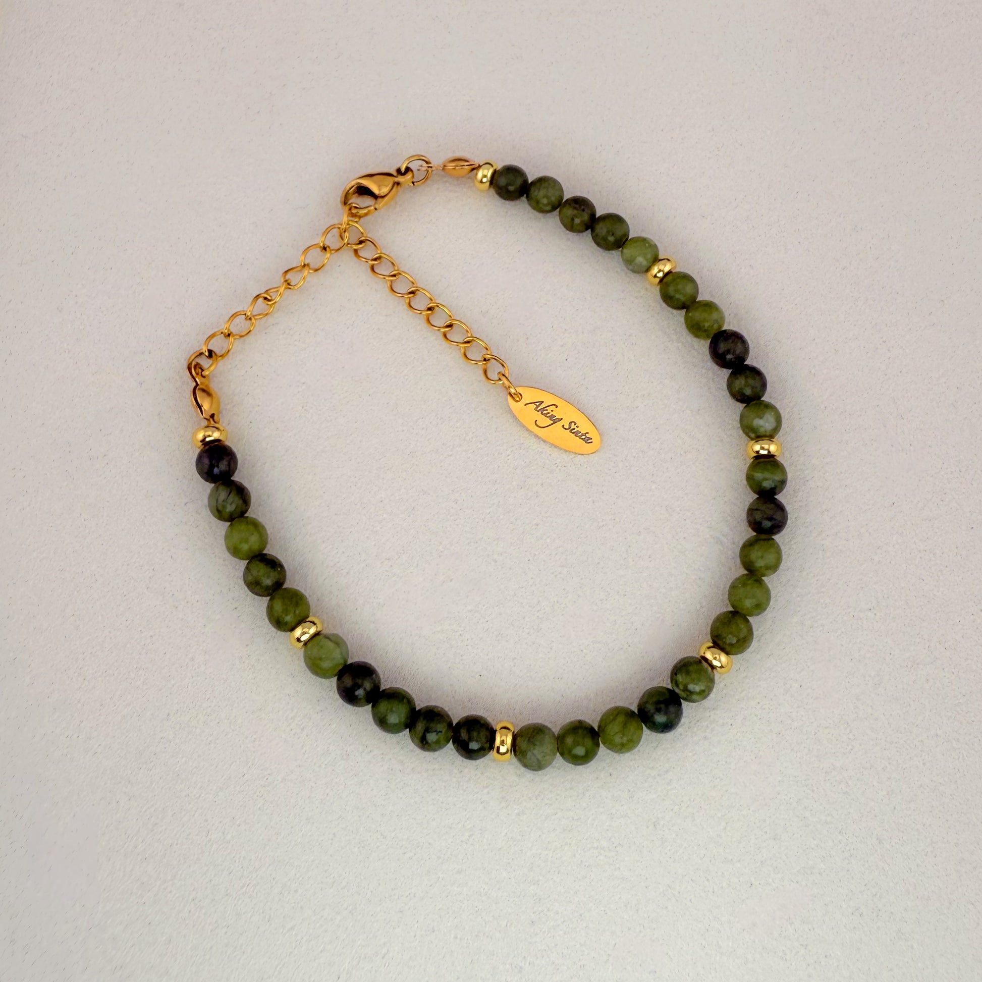 A minimalist Aking Sinta Canadian Jade beaded bracelet without a charm, featuring deep green translucent gemstones and a gold extender chain with a teardrop-shaped metal tag engraved with the "Aking Sinta" brand name.