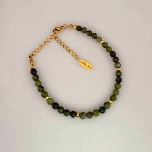 A minimalist Aking Sinta Canadian Jade beaded bracelet without a charm, featuring deep green translucent gemstones and a gold extender chain with a teardrop-shaped metal tag engraved with the "Aking Sinta" brand name.