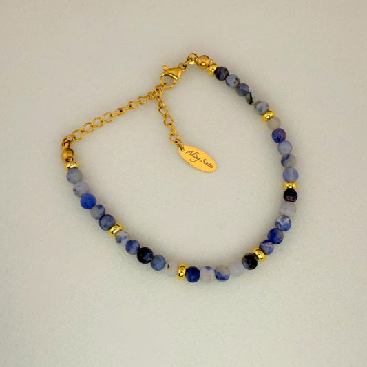 A minimalist Aking Sinta Sodalite beaded bracelet without a charm, featuring navy blue gemstone beads with natural white veins and a gold extender chain with a teardrop-shaped metal tag engraved with the "Aking Sinta" brand name.