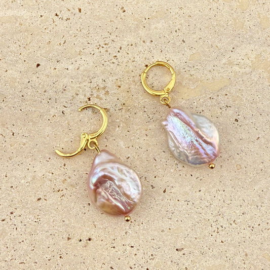Close-up of Aking Sinta purple Keshi pearl huggie earrings on a white stone; one gold hoop is open to show the hinge clasp mechanism.
