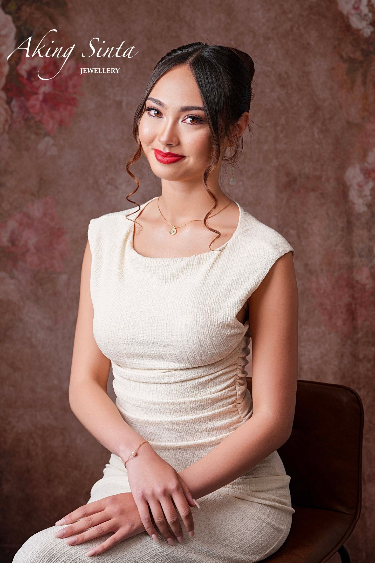 An elegant model sitting and wearing the Aking Sinta Rose and Mother of Pearl necklace; the layered gold floral pendant glows against the skin in a lifestyle setting.