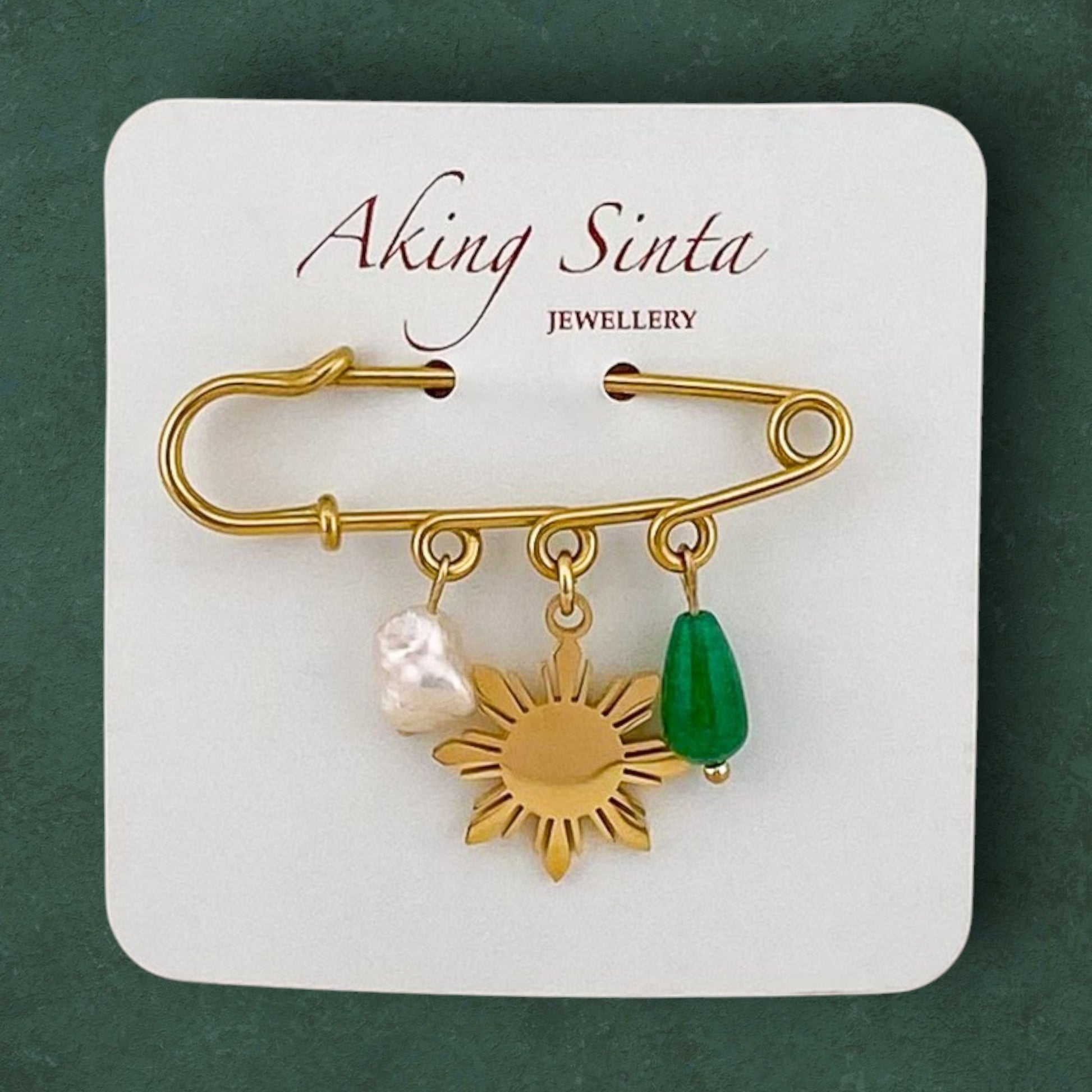 Aking Sinta Safety Pin Brooch with pearl, Araw sun, and jade charms displayed on branded cardboard holder, highlighting intricate design and Philippine-inspired details