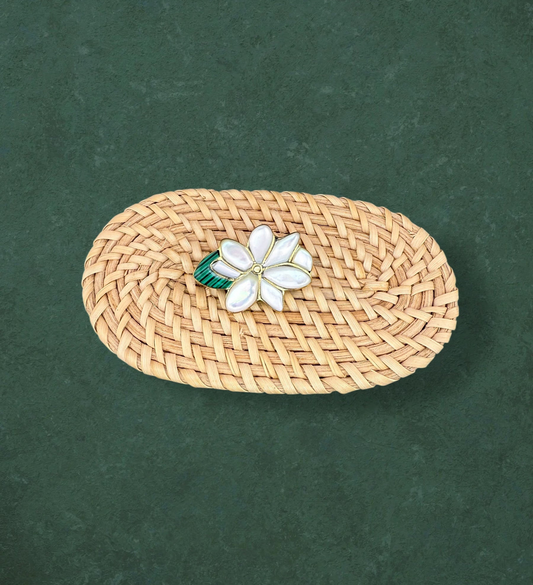 Aking Sinta Sampaguita brooch featuring hand-carved Mother of Pearl petals and a green Malachite center, displayed on a woven rattan surface against a dark green background.