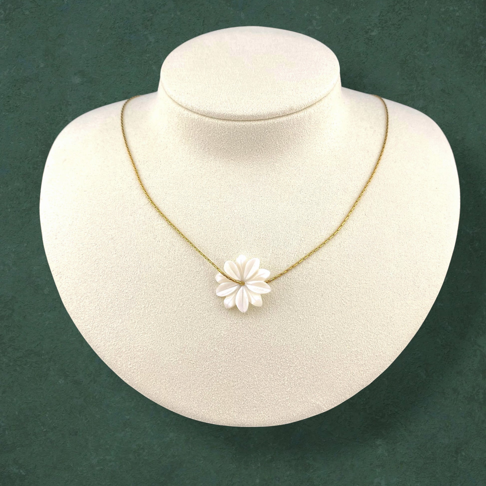 Aking Sinta Floating Sampaguita necklace featuring a carved Mother of Pearl flower bud on a gold chain, displayed on a white bust against a dark green background.