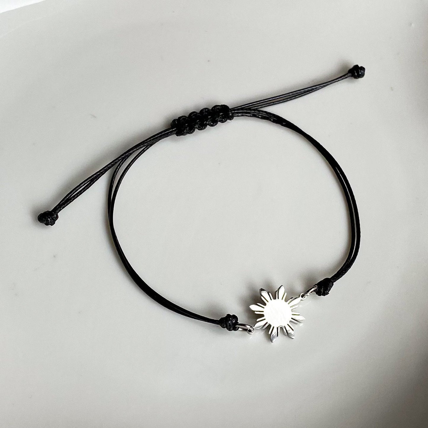 Aking Sinta unisex friendship bracelet featuring a polished silver 8-ray Philippine sun charm on a durable black cord; displayed on a white background to emphasize the sharp contrast and modern design.
