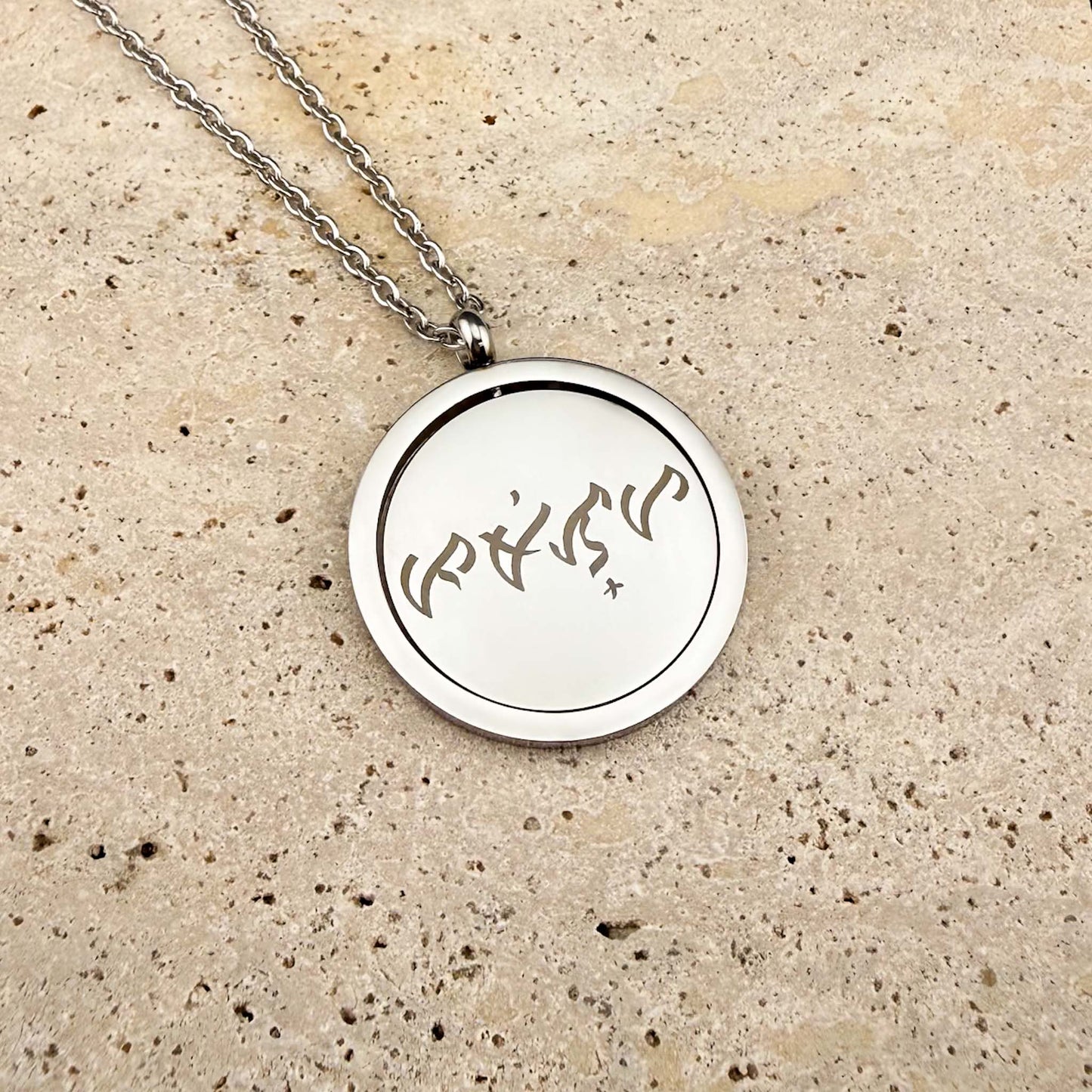 Close-up of the Aking Sinta silver Spinning Coin necklace featuring bespoke Baybayin script engraving, displayed on a polished white marble slab.