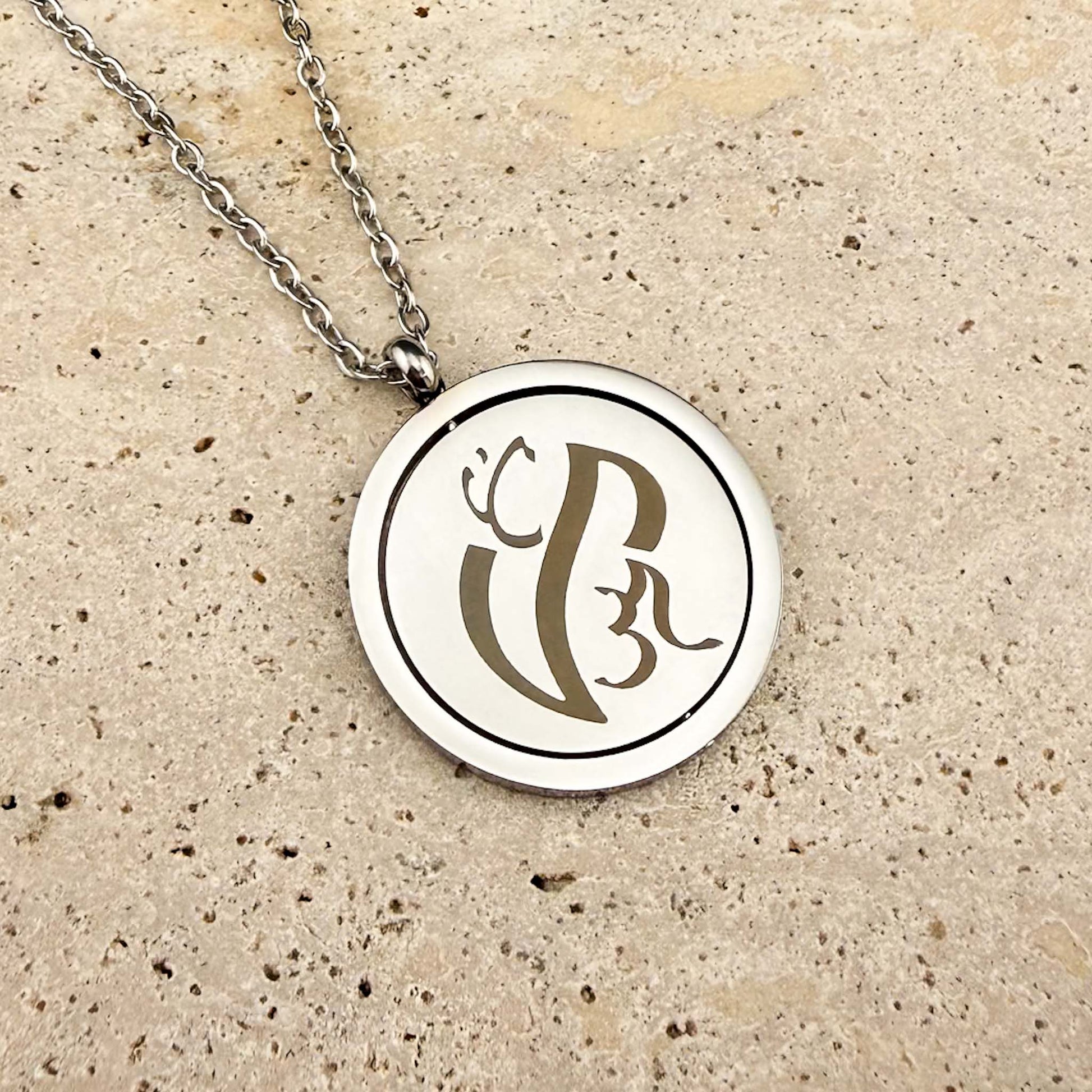 Close-up of a silver Aking Sinta Spinning Coin necklace on marble, featuring a unique variant of bespoke Baybayin script engraving.