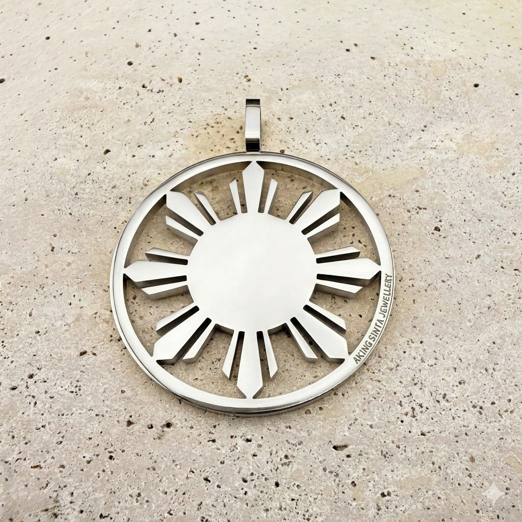 A detailed close-up of a polished silver Aking Sinta statement Araw medallion, featuring a crisp, laser-cut sun design. The sleek, modern piece is presented on a light, textured natural stone surface, highlighting the minimalist and bold aesthetic of the brand