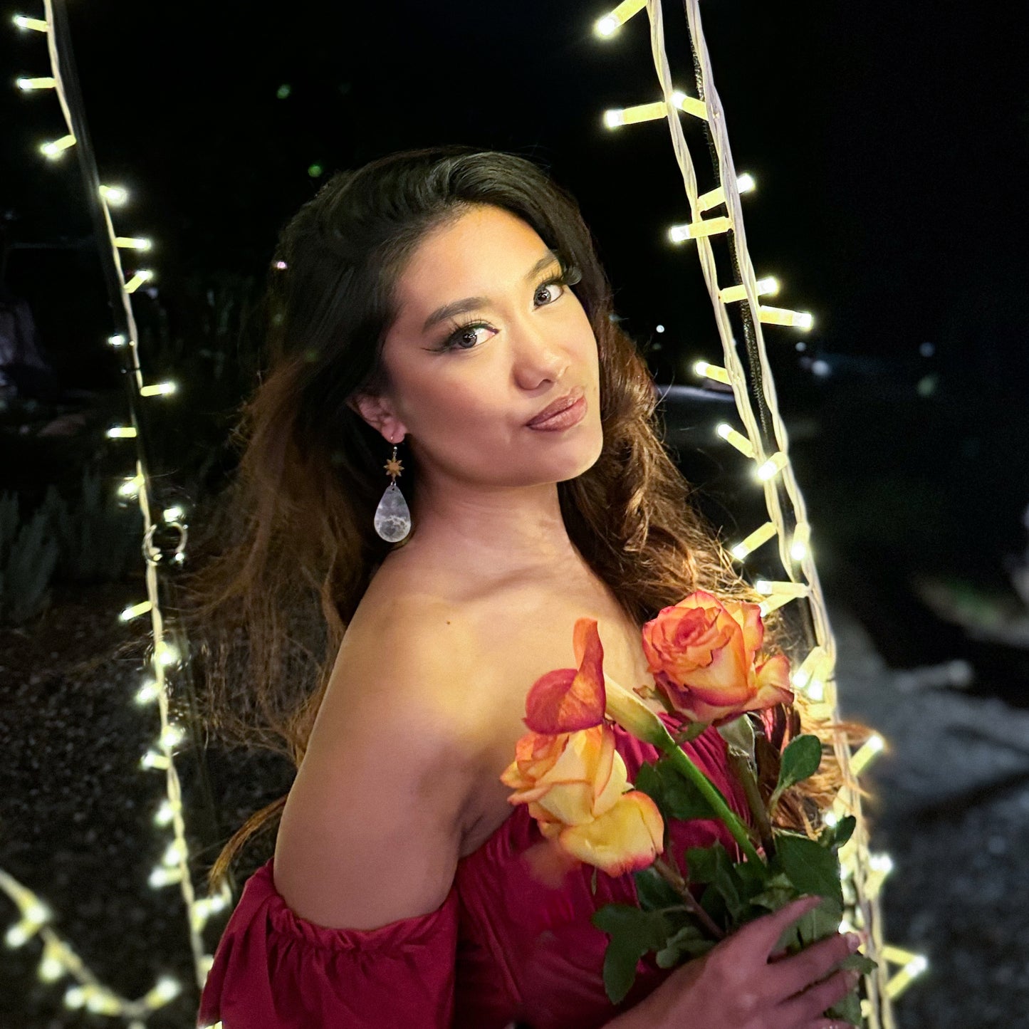 Aking Sinta Teardrop Capiz Shell Hook Earrings with Araw charms worn by woman in red dress holding a flower with Christmas lights background