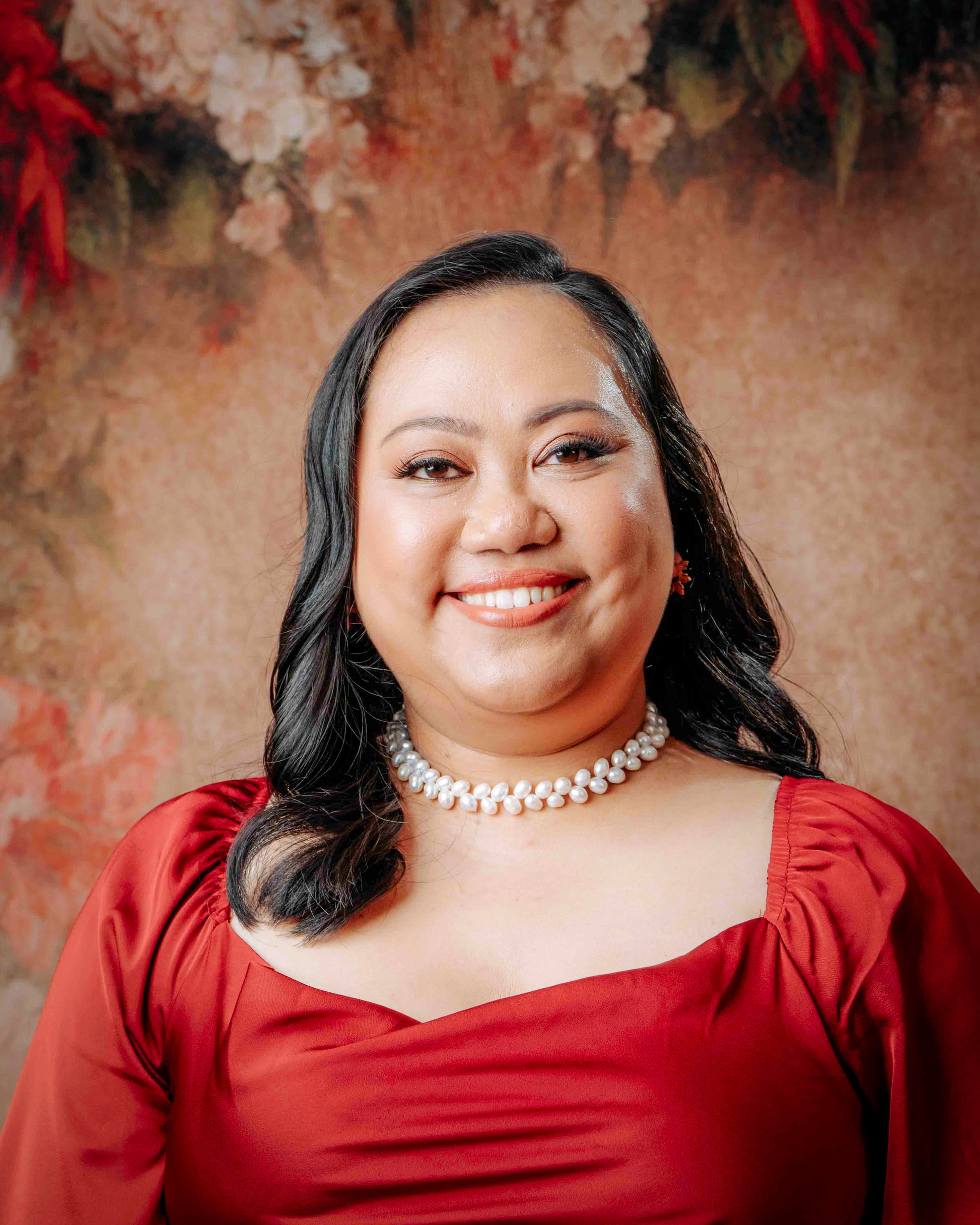 Close-up lifestyle shot of a model in a vibrant red dress wearing the Aking Sinta Wheat Pearl Necklace, highlighting the contrast between the white pearls and the bold fabric.