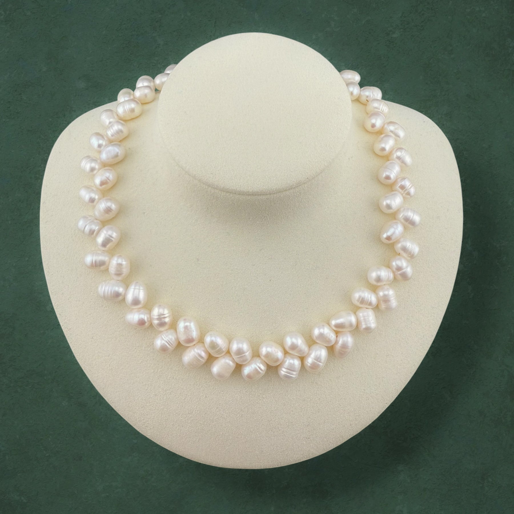 Aking Sinta Wheat Pearl Necklace featuring a textured, grain-stalk arrangement of rice pearls, displayed on a white jewelry bust against a dark green background.