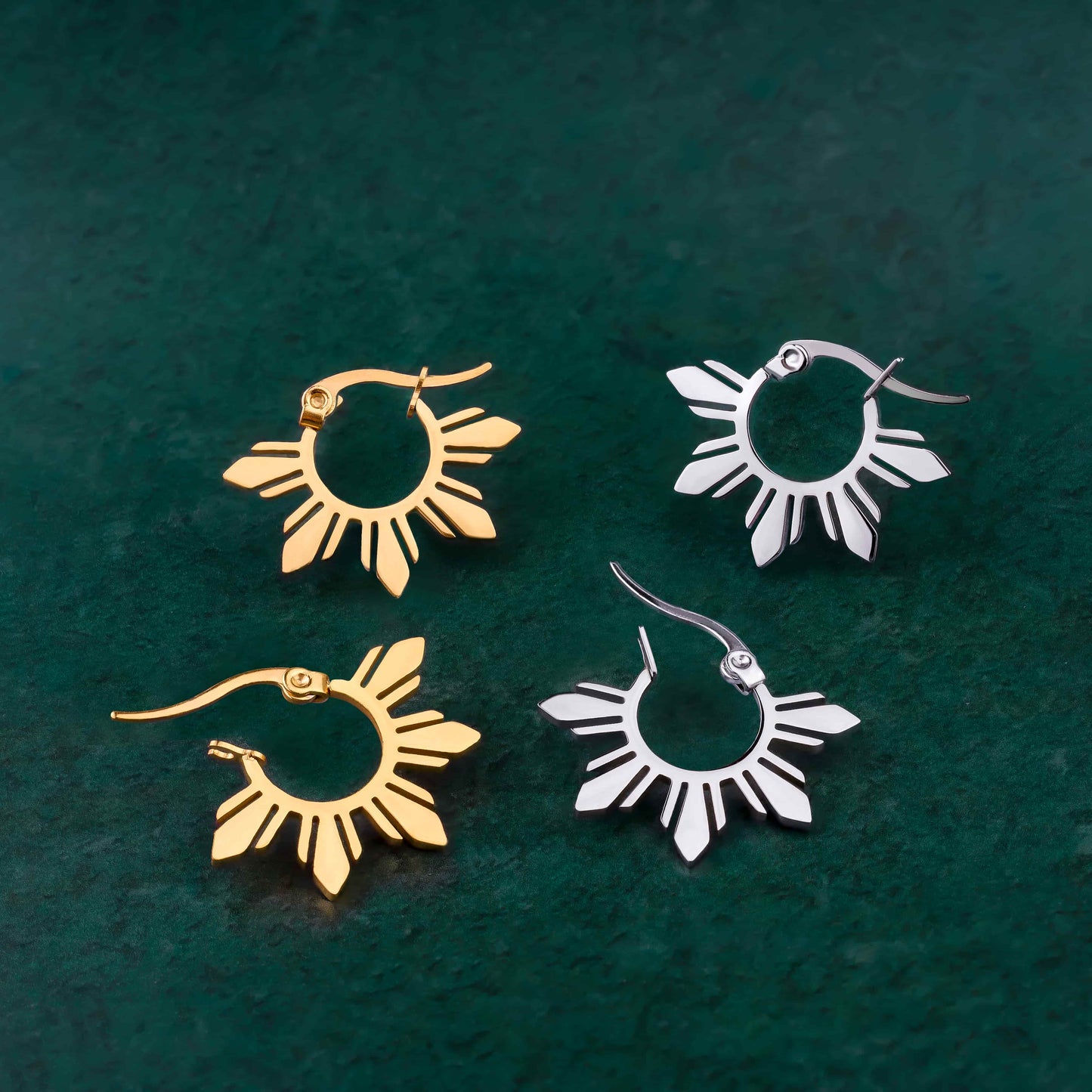 Pair of Araw hoop earrings in gold and silver featuring 5-ray sunburst details, displayed on a minimalist solid green background for modern jewelry styling.