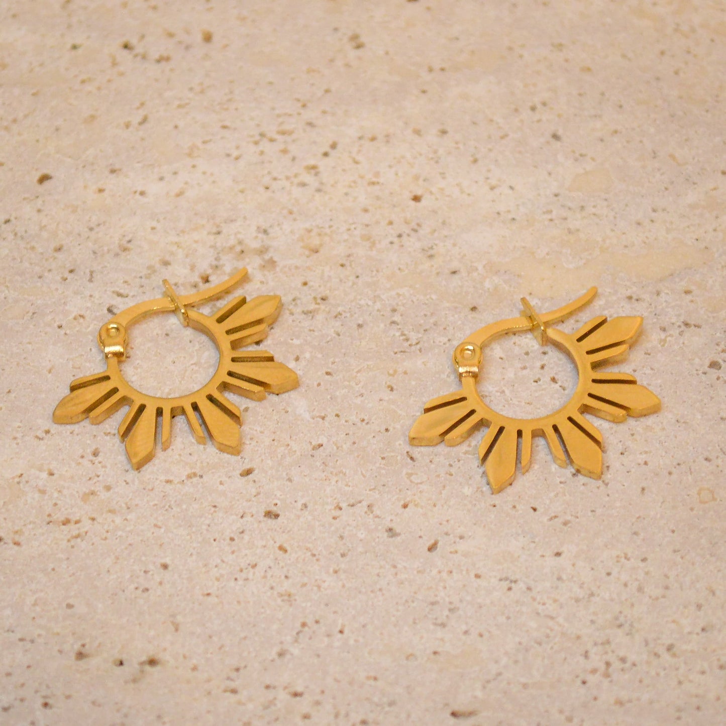 A pair of Araw gold sun hoop earrings with a 5-ray design displayed on a white marble background, showcasing the warm gold tones and premium minimalist aesthetic.