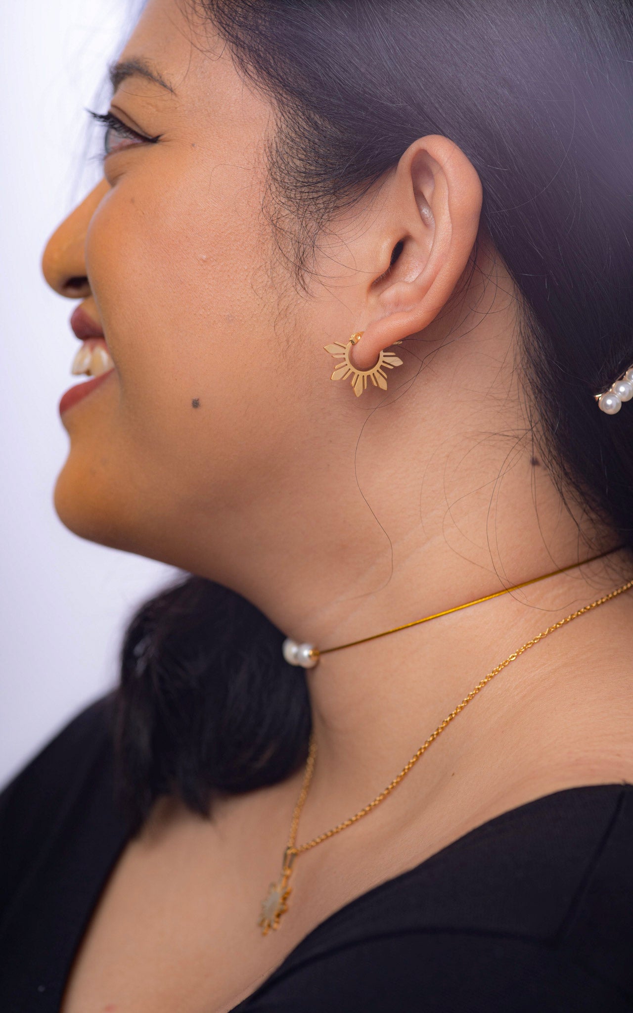 Side view of a model wearing Araw gold 5-ray sun hoop earrings against black clothing, highlighting the golden sunburst silhouette and elegant profile