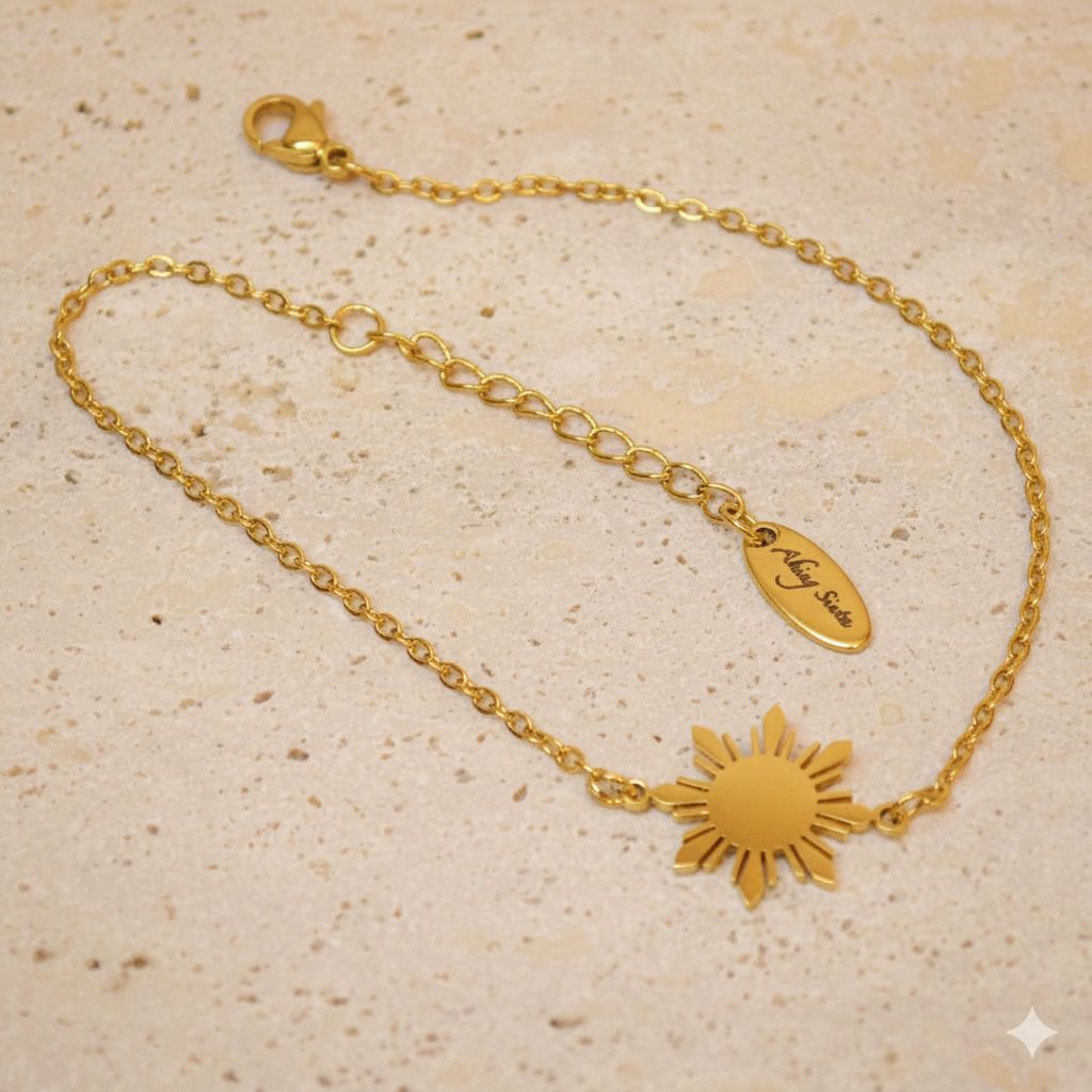 Complete close-up of the Araw gold sun jewelry variant on a white marble background, highlighting the rich gold luster and detailed 5-ray sunburst engraving