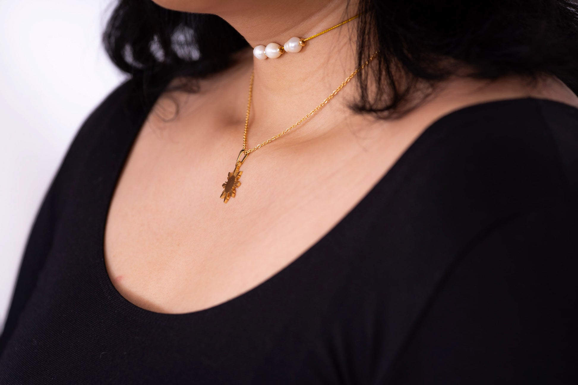 Araw minimalist gold sun pendant necklace highlighted on a woman wearing a black outfit, elegant high-contrast jewelry photography for evening style.