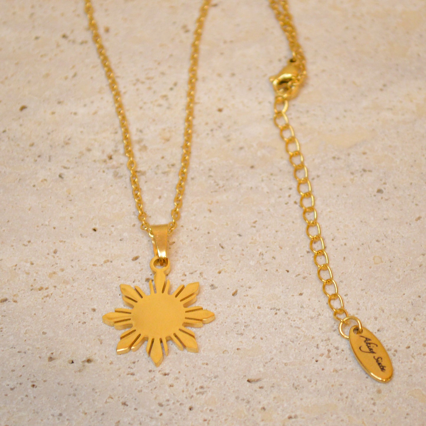 Full view of the Araw minimalist gold sun necklace with a delicate gold chain, displayed on a premium white marble background showing the complete jewelry piece.