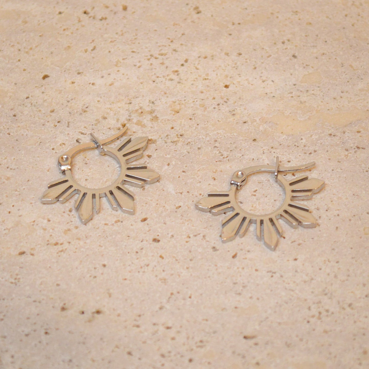 A pair of silver Araw 5-ray sun hoop earrings on a white marble background, featuring a polished silver finish and minimalist celestial silhouette