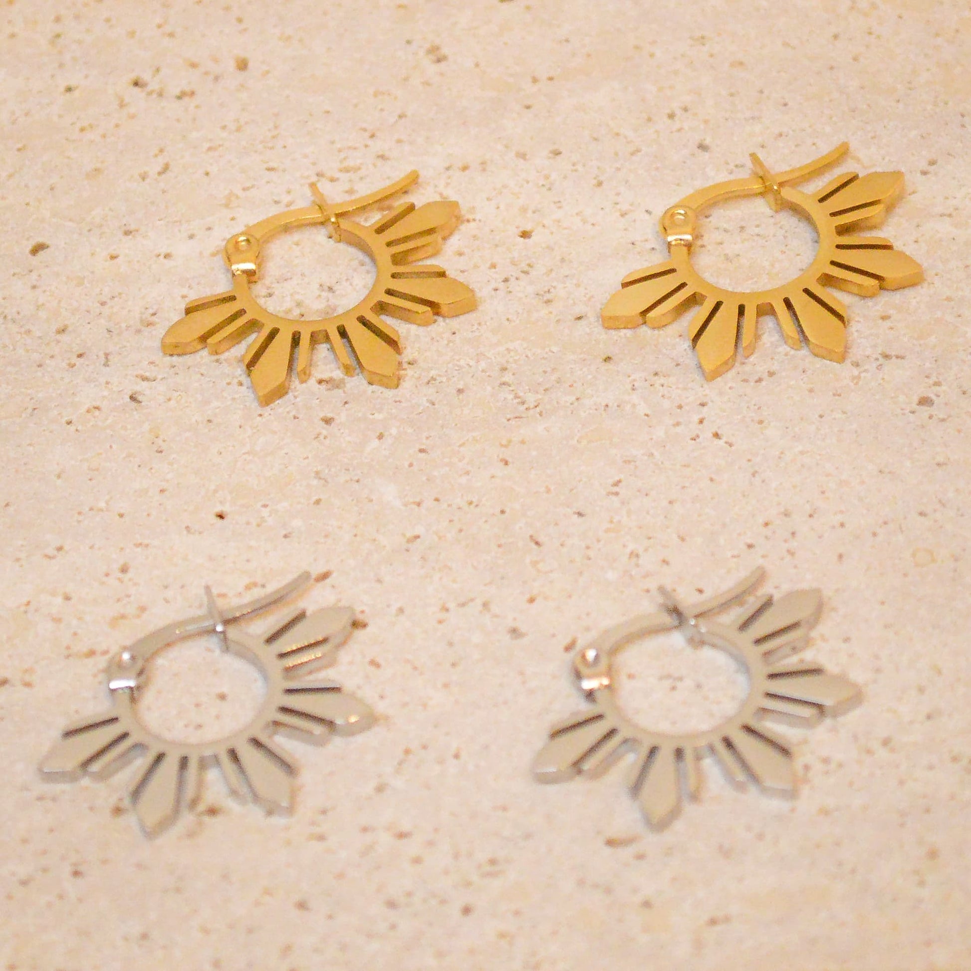 A pair of silver Araw 5-ray sun hoop earrings displayed on a white marble background, showcasing the sleek polished finish and modern celestial design
