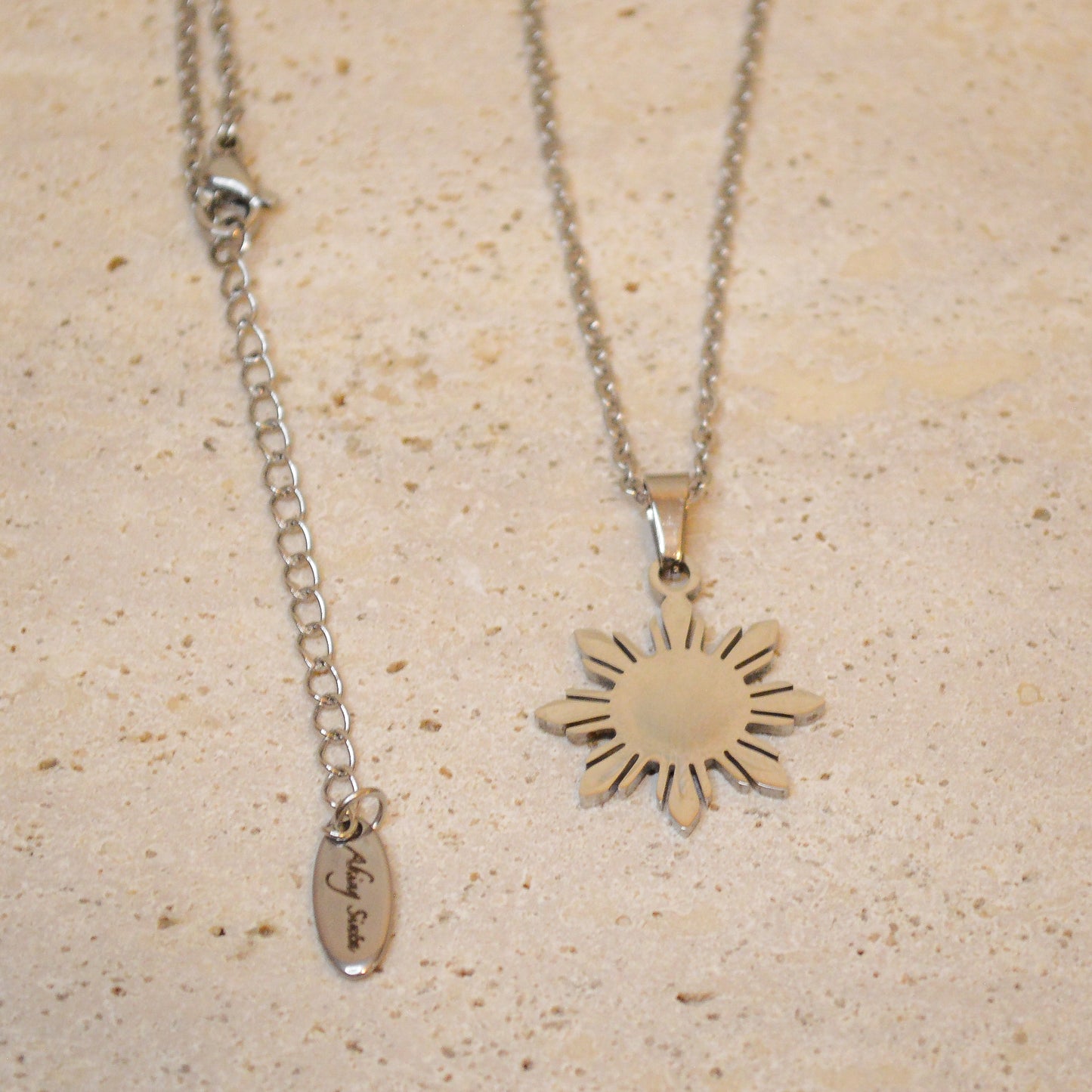 Full view of the Araw minimalist silver sun necklace with dainty chain, displayed on a white marble background to show complete jewelry design and length.