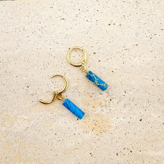 Gold circular ocean blue Imperial Jasper earrings on marble, showing one huggie clasp open to reveal the hinge and post.