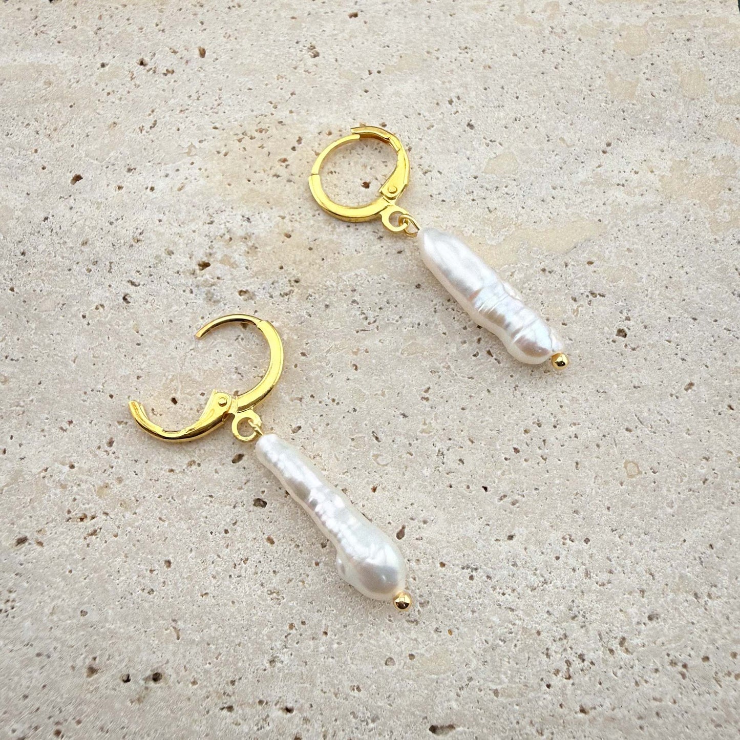 Gold stick baroque pearl earrings on marble, showing one huggie hoop open to display the hinge clasp mechanism.