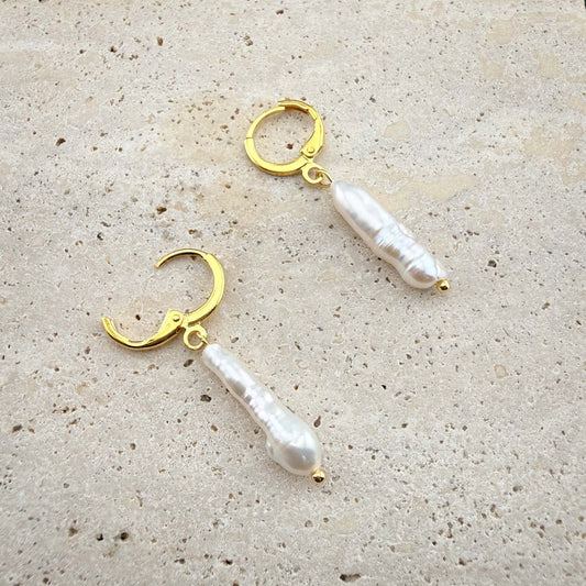 Gold stick baroque pearl earrings on marble, showing one huggie hoop open to display the hinge clasp mechanism.